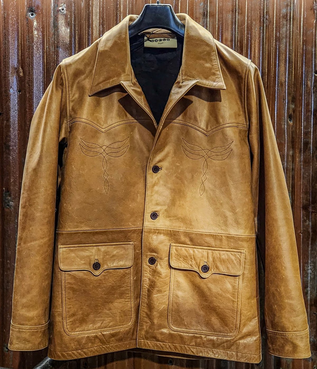 Suede tan jacket with embroidered detailing on display against a wooden background.