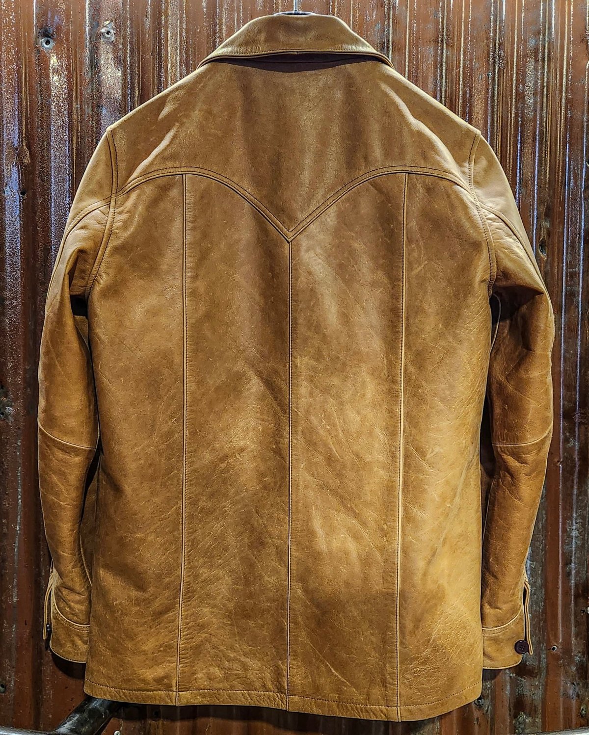 Suede tan jacket with embroidered detailing on display against a wooden background.